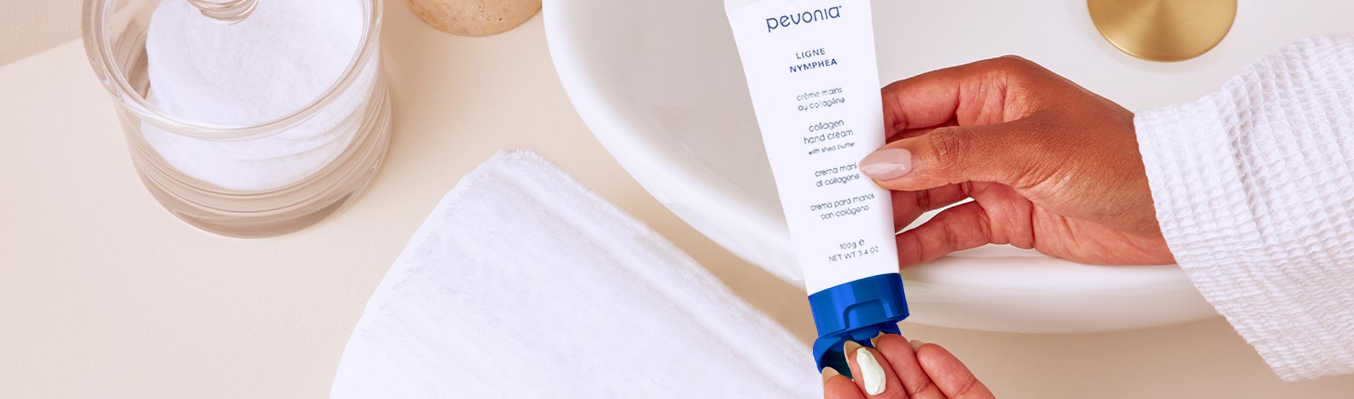 Pevonia's Collagen Hand Cream being squeezed into someone's hand over a sink and towel.