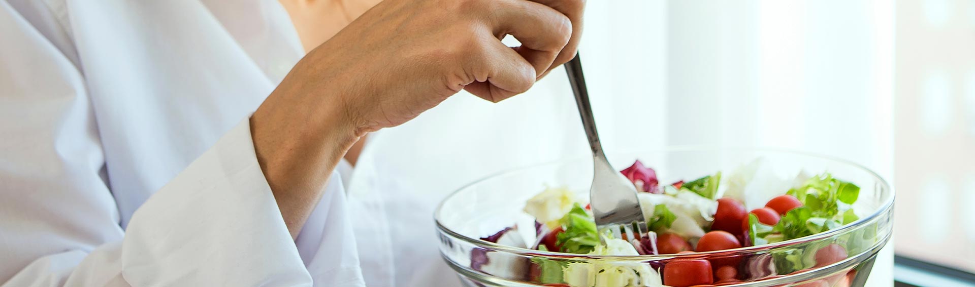 Woman eating a salad out of a clear glass bowl.